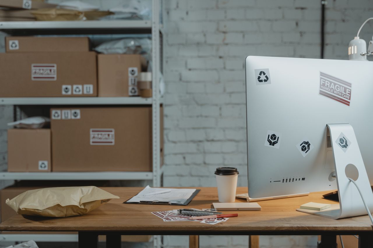 Contemporary office setup with a computer, coffee, and parcels on a wooden desk.